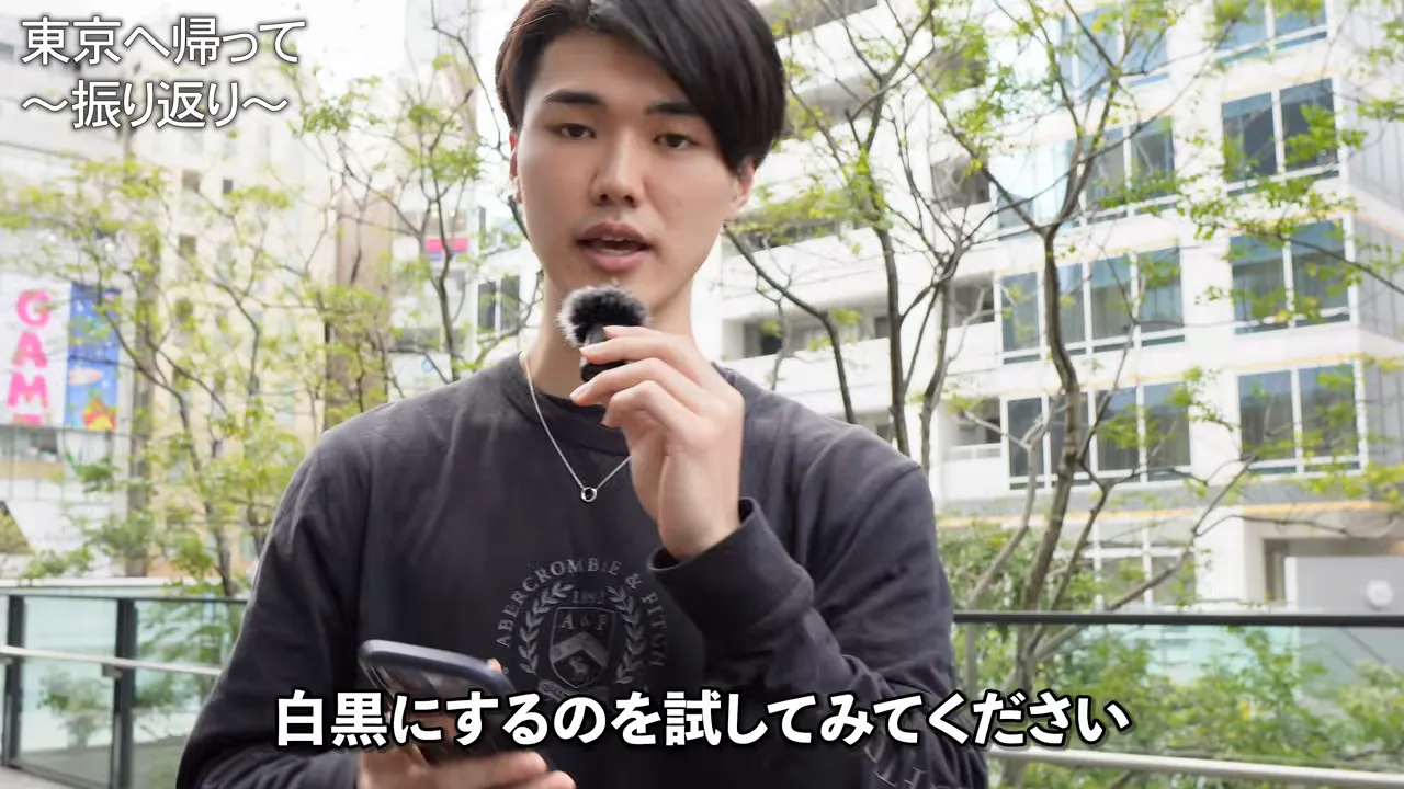 街中で携帯を手に持ちながら、「白黒にするのを試してみてください」という字幕が出ている場面