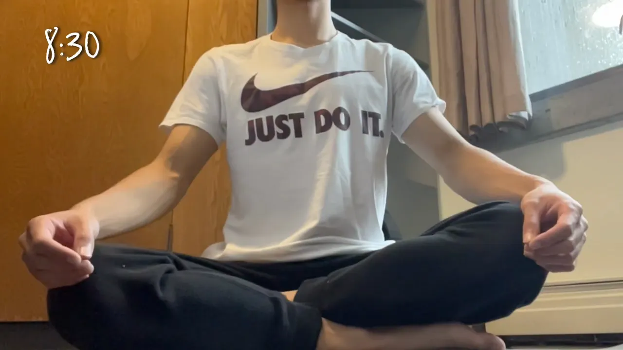 「JUST DO IT」と書かれた白いTシャツを着て、床にあぐらを組んで瞑想している様子。左上に8:30の時刻